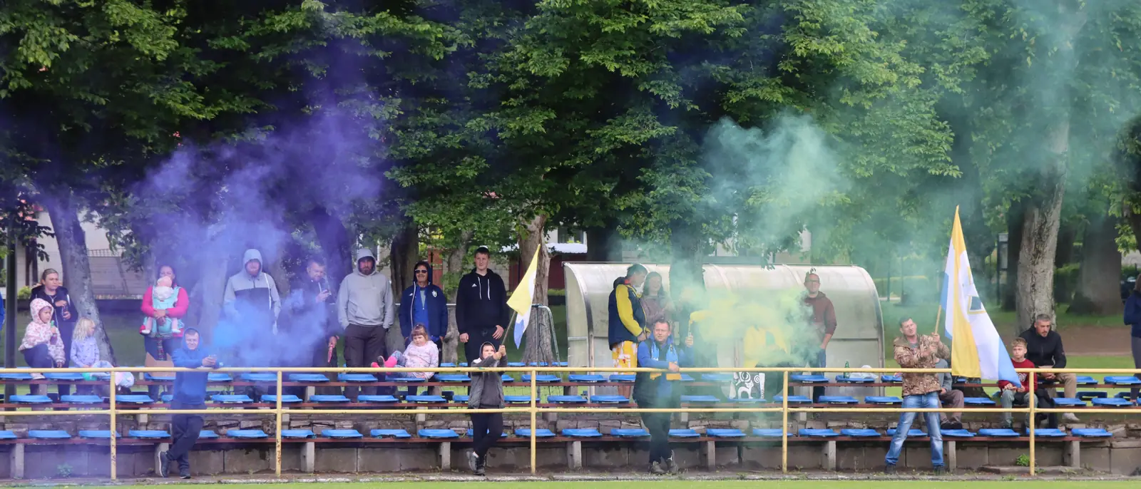 Trybuna stadionu w Choczewie pełna kibiców, nad nią dym w barwach klubu